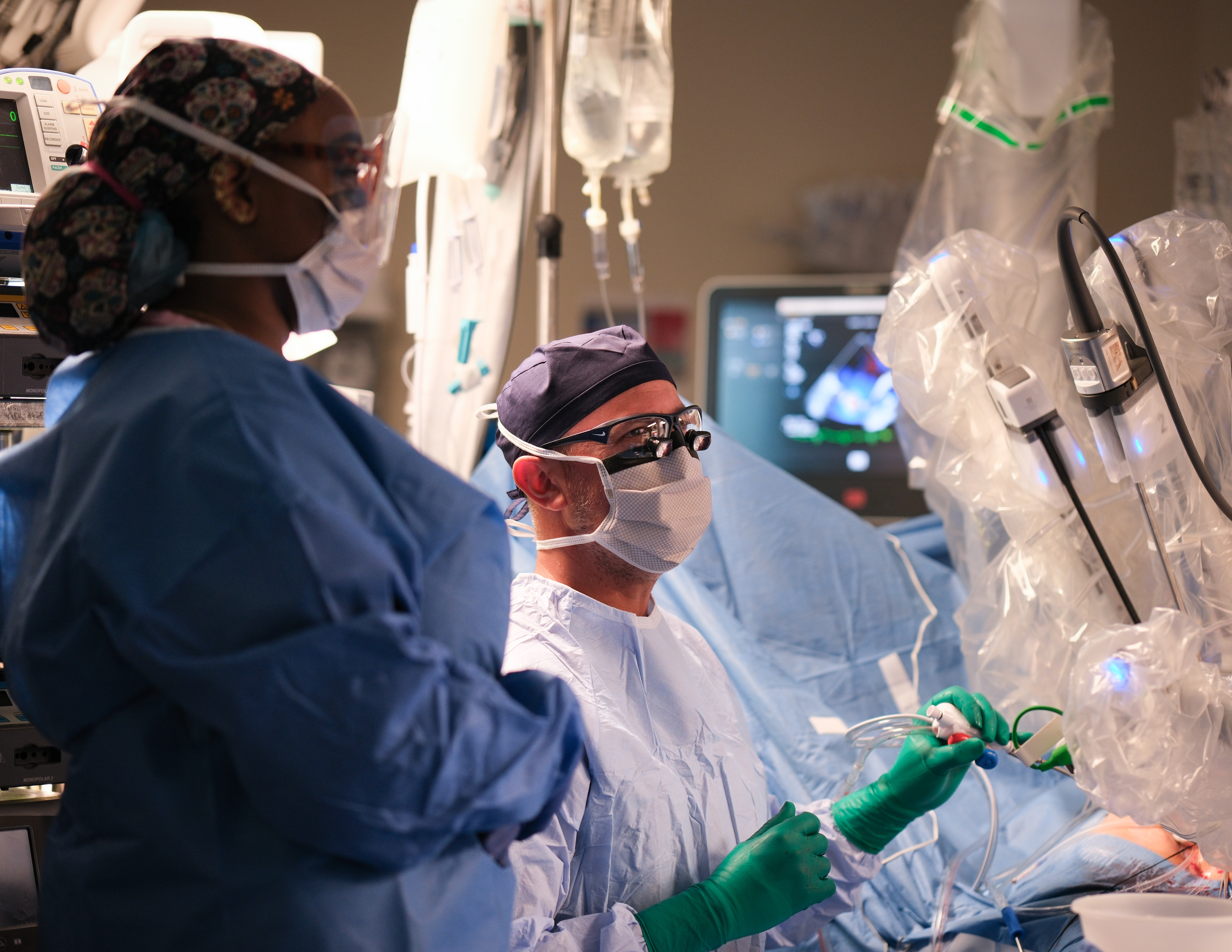 Photo of healthcare providers in surgical gowns manipulating controllers for a robotic heart surgery