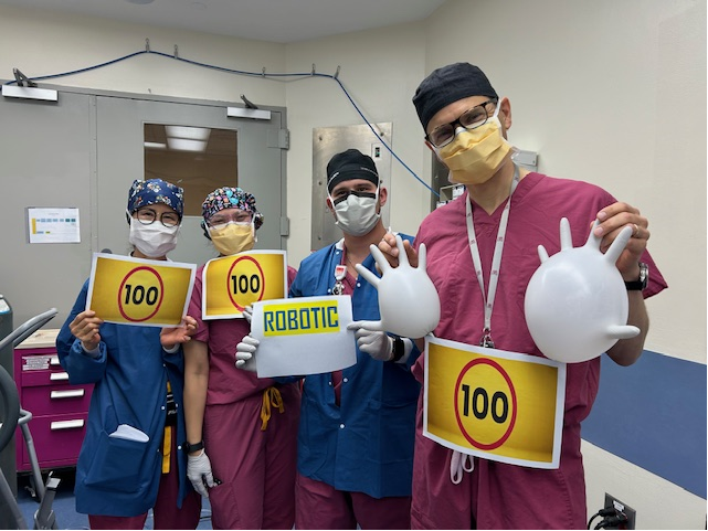 surgery team stands outside the OR holding signs to mark the 100th robotic heart surgery