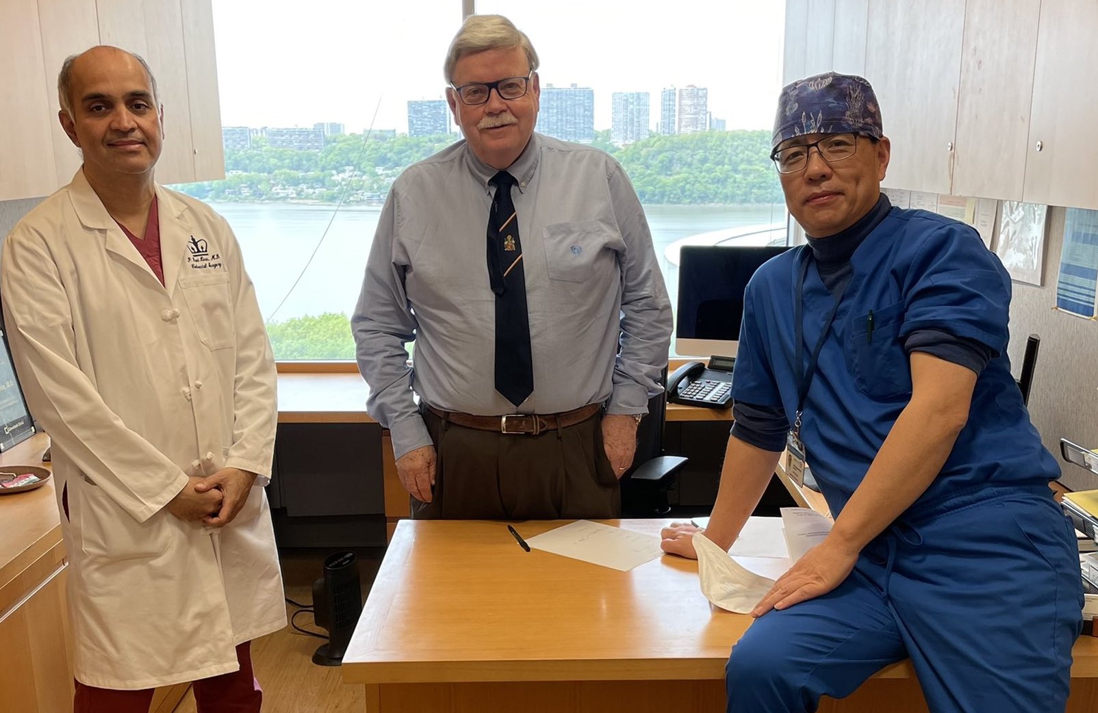 Drs. Kiran, Church, and Shen stand around a desk in the hospital.