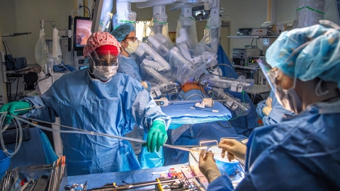 Photograph showing medical staff performing robotic surgery in an operating room.